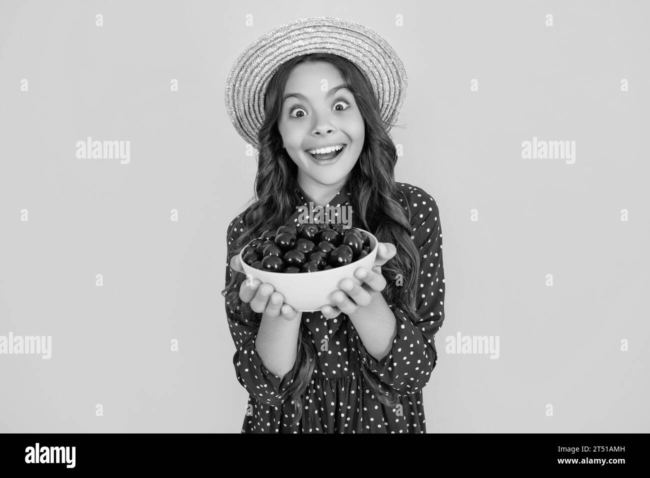 enfant de l'adolescence émerveillé tient le bol de cerise sur fond jaune Banque D'Images
