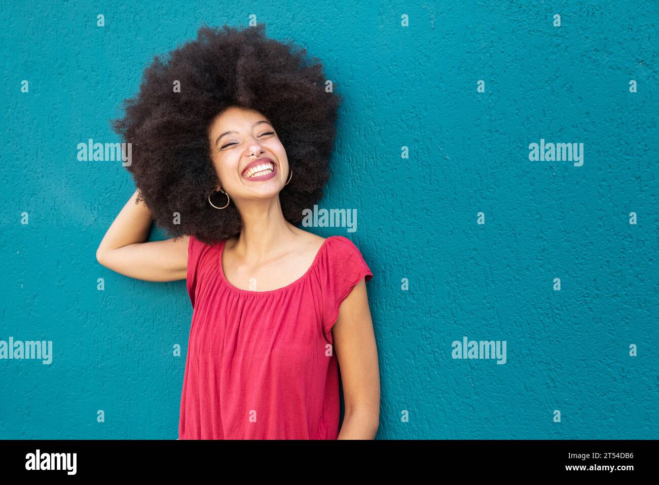 Portrait de femme marocaine souriante dans des vêtements décontractés avec coiffure afro debout contre le mur bleu vif Banque D'Images