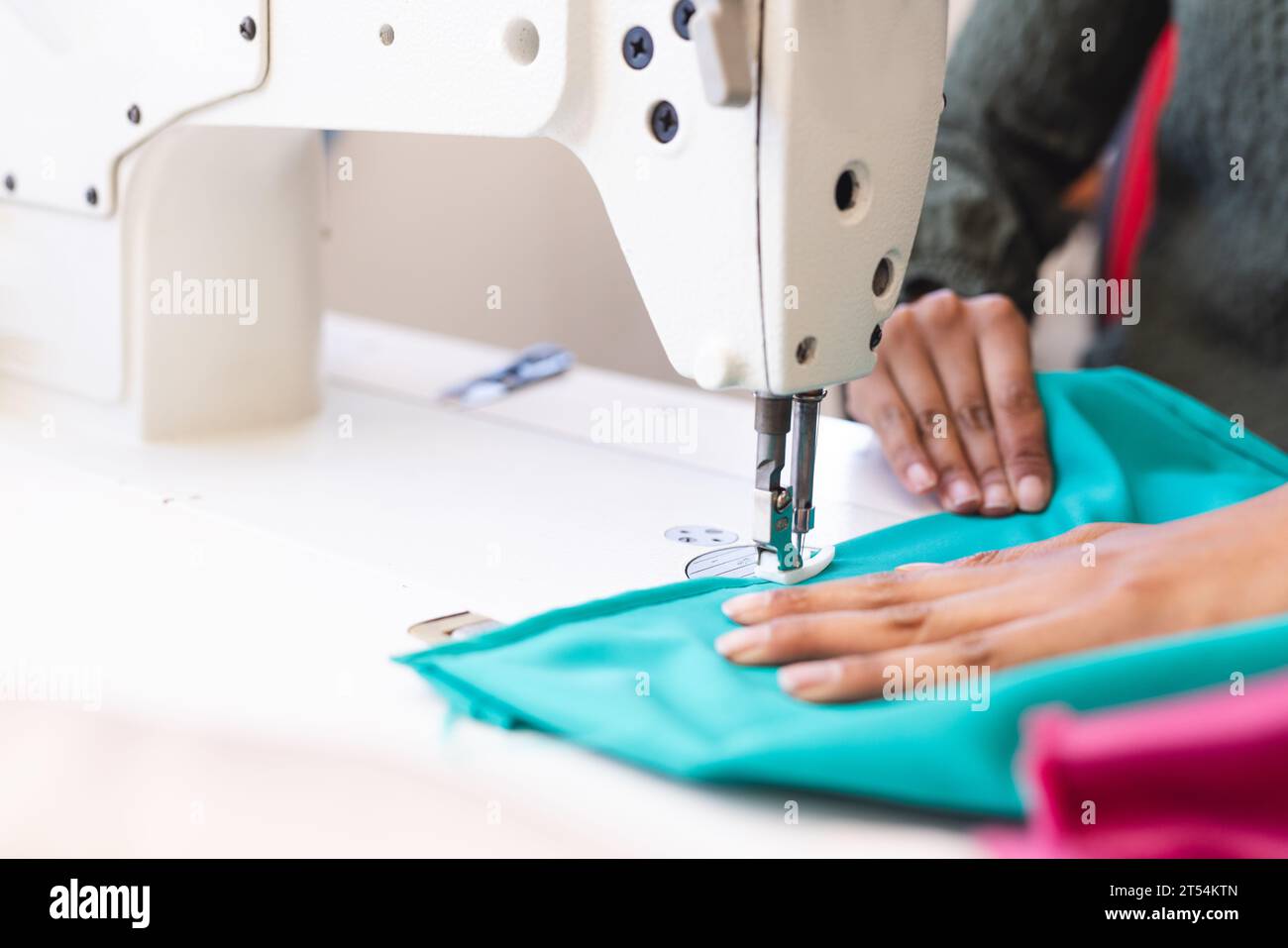 Créateur de mode féminin biracial utilisant la machine à coudre dans le studio ensoleillé Banque D'Images