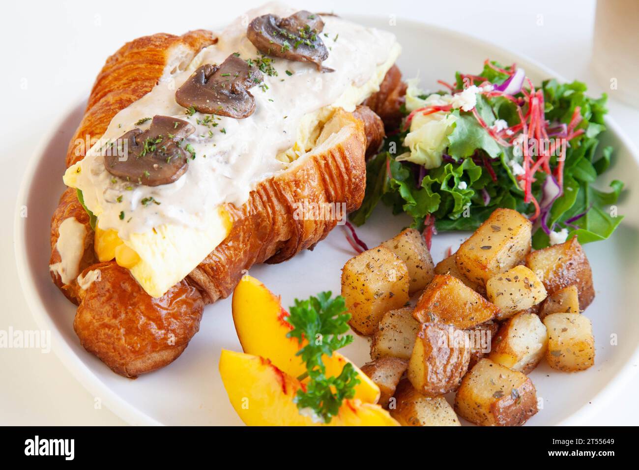 Sandwich au fromage à la crème aux champignons et aux croissants briochés aux œufs brouillés avec pêche, feta aux feuilles de roquette et pommes de terre sautées. Banque D'Images