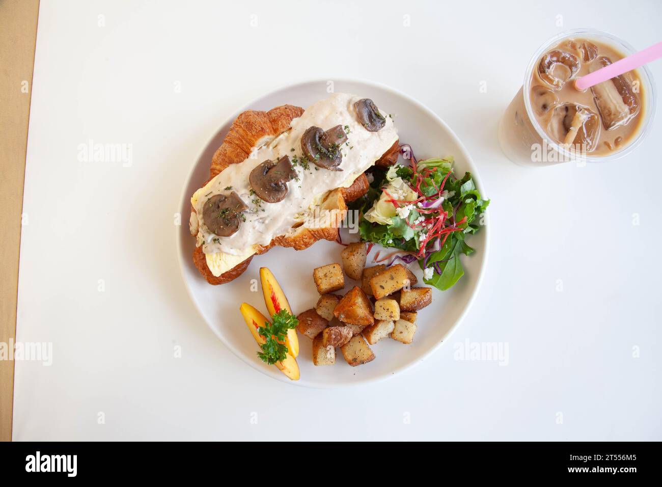 Sandwich au fromage à la crème aux champignons et aux croissants briochés aux œufs brouillés avec pêche, feta aux feuilles de roquette et pommes de terre sautées avec latte glacé. Banque D'Images