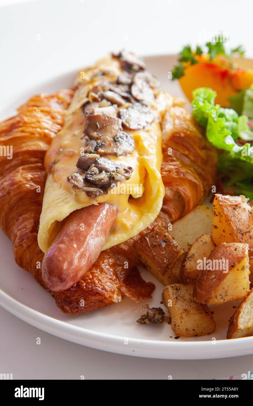 Sandwich brioche aux œufs croissants et saucisses avec fruits et légumes frais dans un café. Banque D'Images