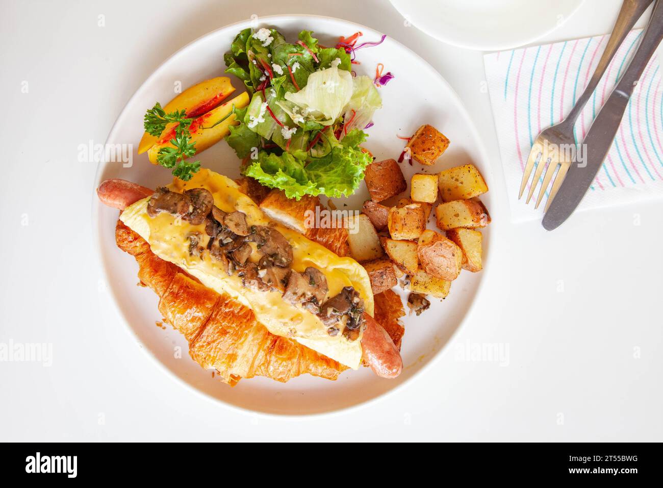 Sandwich brioche aux œufs croissants et saucisses avec fruits et légumes frais dans un café. Banque D'Images