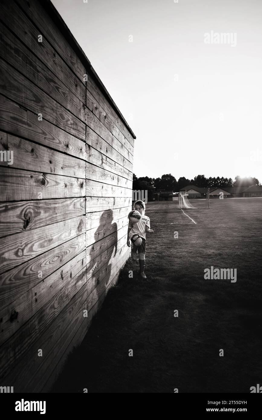 Jeune fille dribbling ballon de football sur le terrain au coucher du soleil Banque D'Images