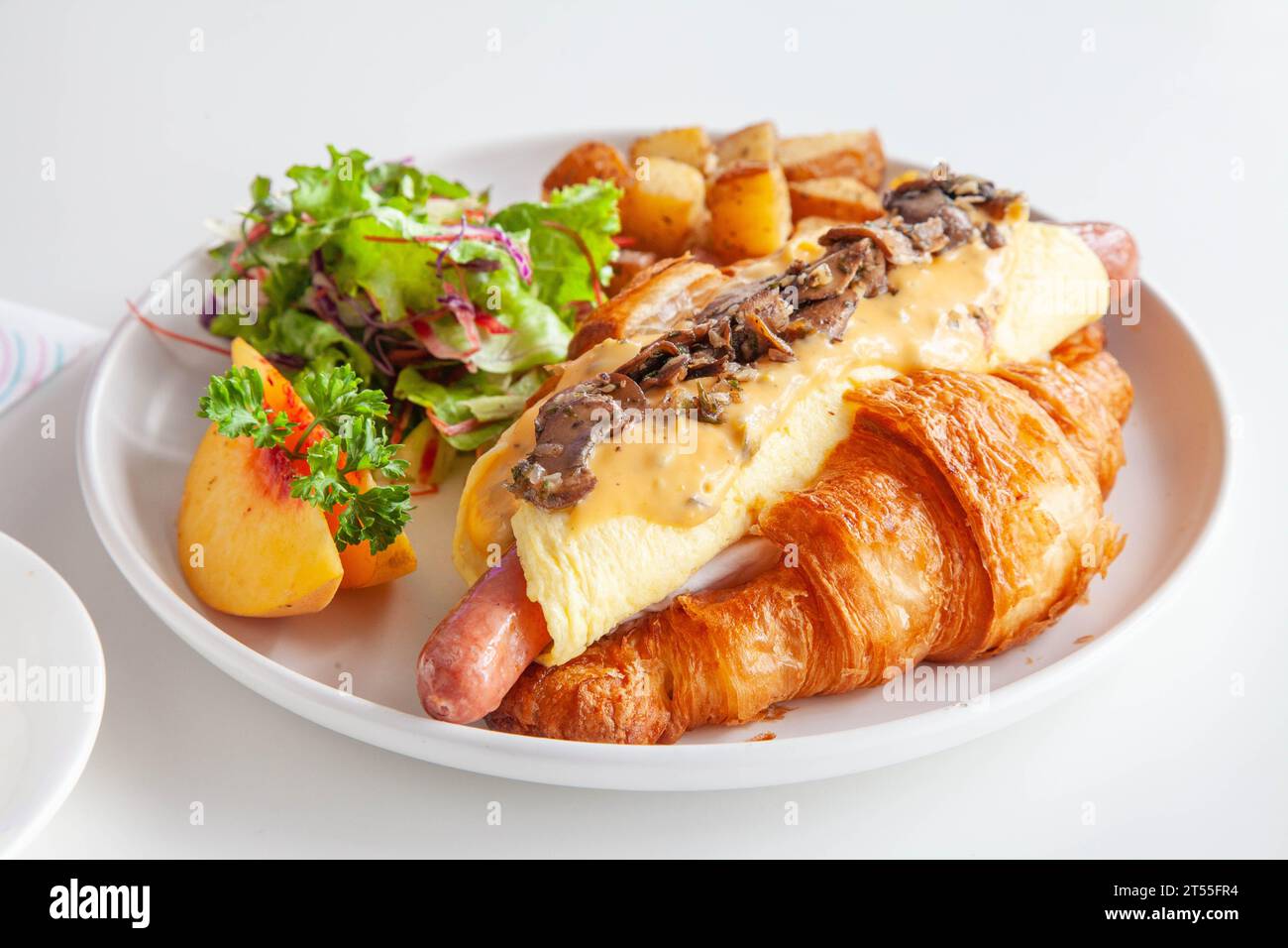Sandwich brioche aux œufs croissants et saucisses avec fruits et légumes frais dans un café. Banque D'Images