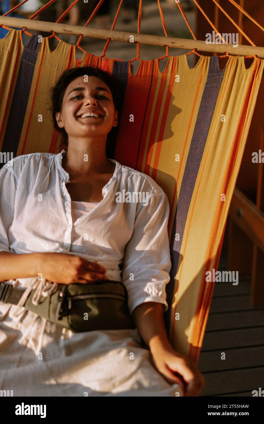 Jeune femme heureuse allongée sur un hamac rayé coloré. Banque D'Images