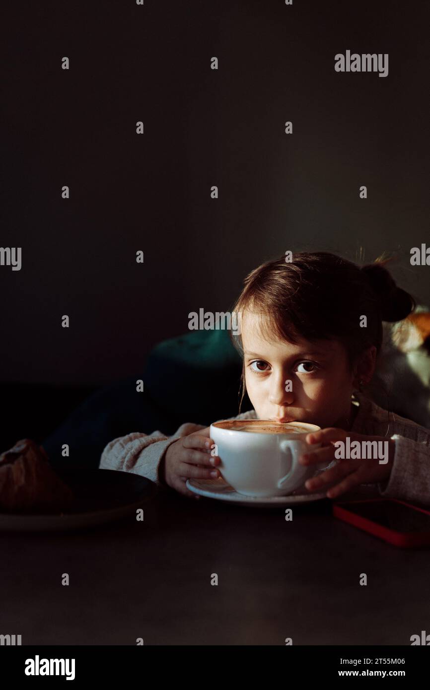 Une fillette boit du cacao dans un café. Banque D'Images