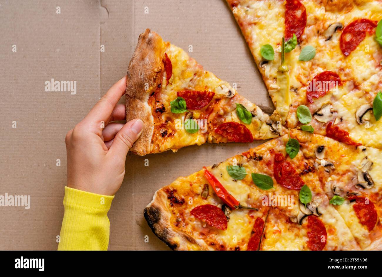 La main féminine prend un morceau de pizza. Vue à angle élevé de pizza au pepperoni et basilic. Banque D'Images