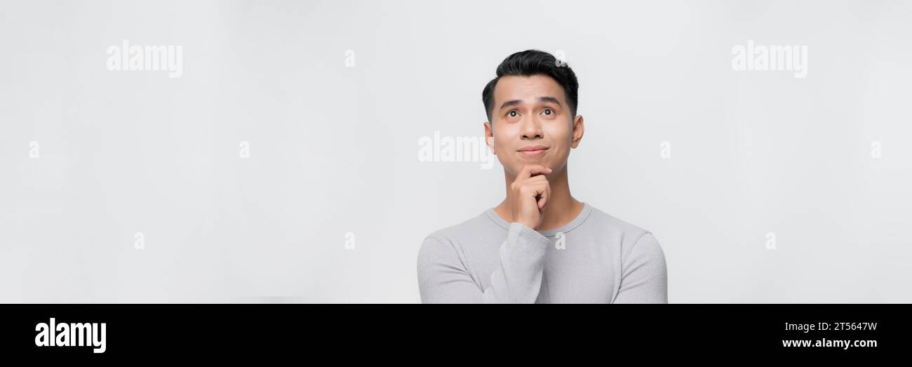 Bannière d'un homme d'affaires asiatique regardant vers le haut pensant main sur le menton, isolé sur fond blanc. Banque D'Images
