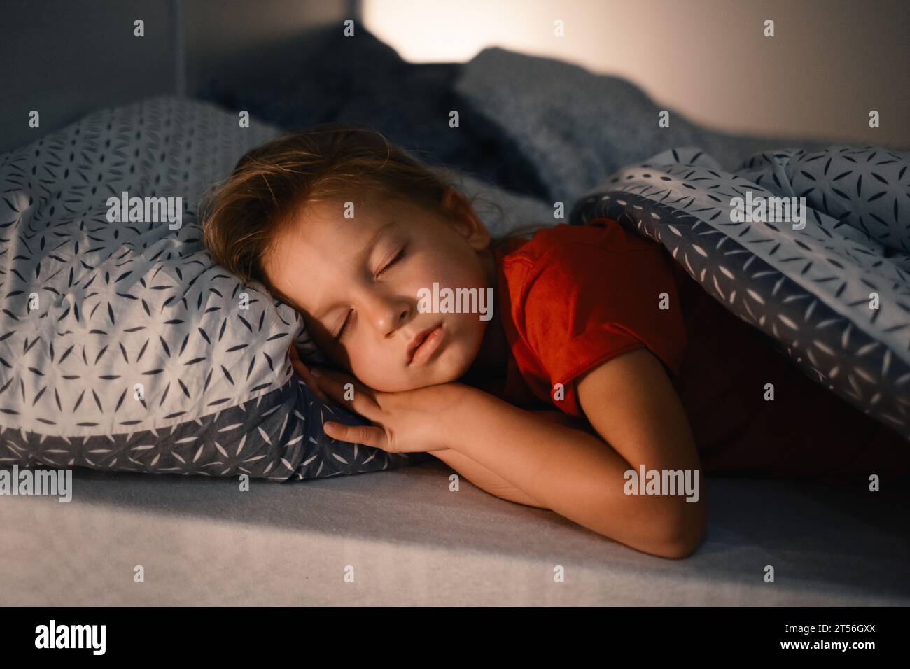 Enfant dormant dans le lit tard dans la nuit. Coussin mignon pour petite fille recouvert d'une couverture chaude. Enfant ayant le repos de nuit. Lumière sur la table de nuit Banque D'Images
