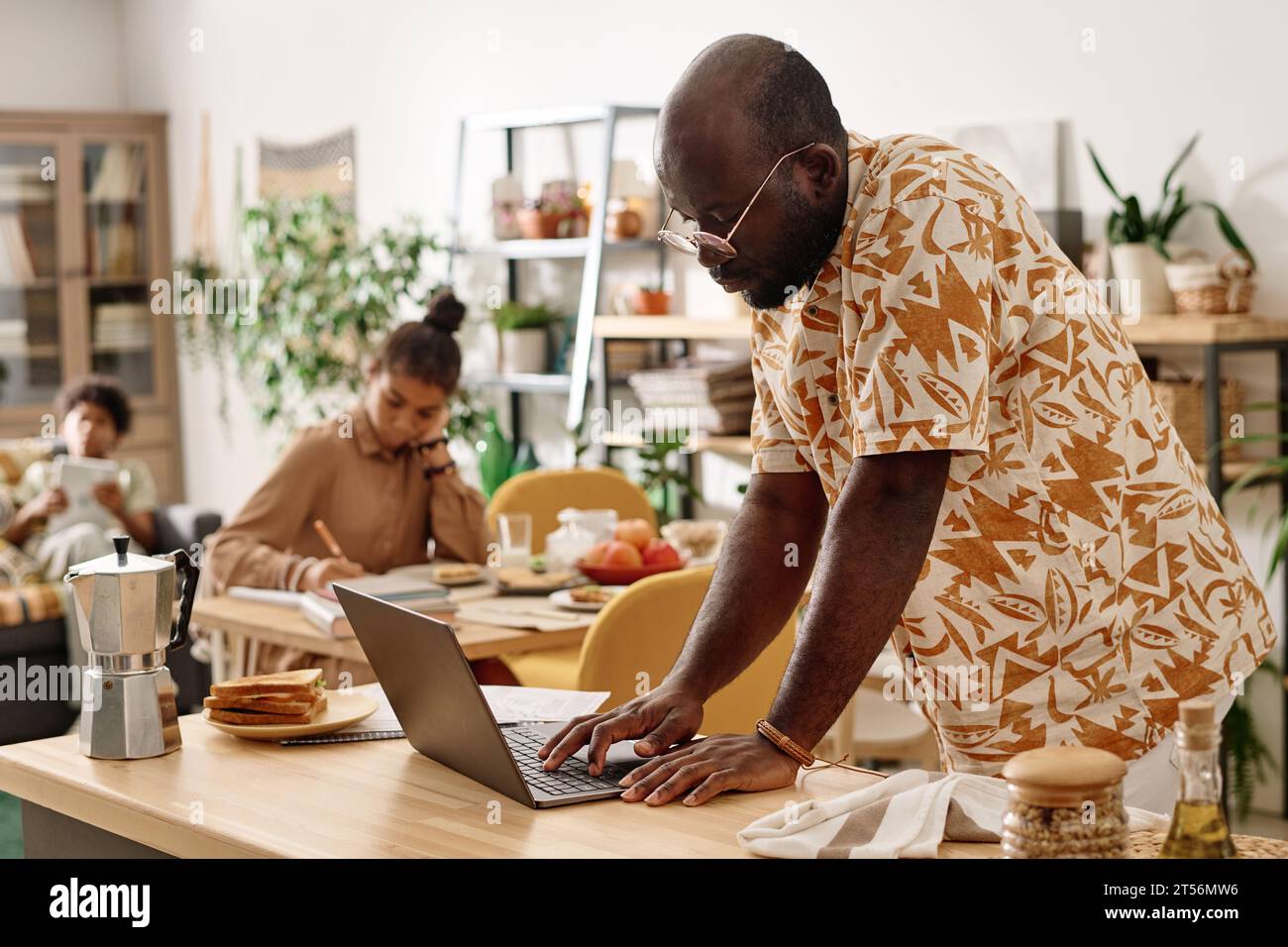 Homme noir sérieux dans les lunettes vérifiant les e-mails sur ordinateur portable lorsqu'il travaille à domicile le week-end Banque D'Images