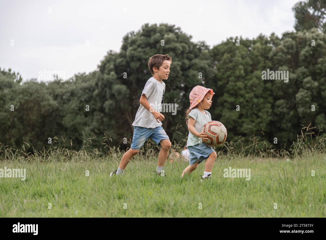 Deux enfants jouant avec un ballon dans le parc verdoyant. Concept d'enfance heureuse au contact de la nature, mode de vie sain. Banque D'Images