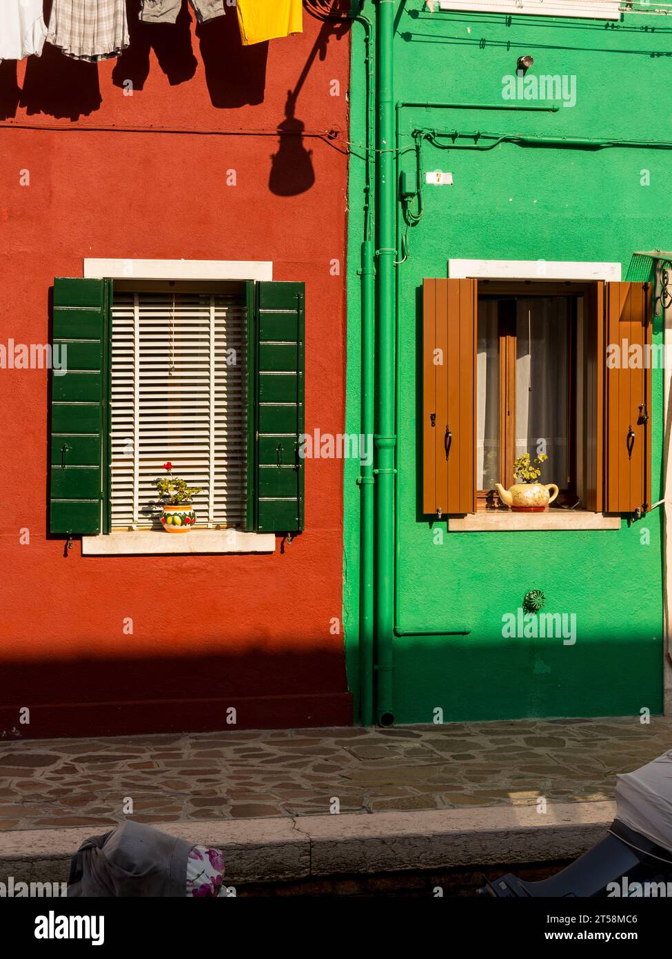 Contraste entre deux maisons à Burano, Venise, Italie. Une couleur rouille et l'autre verte. Des pots de fleurs ornent les fenêtres. Banque D'Images