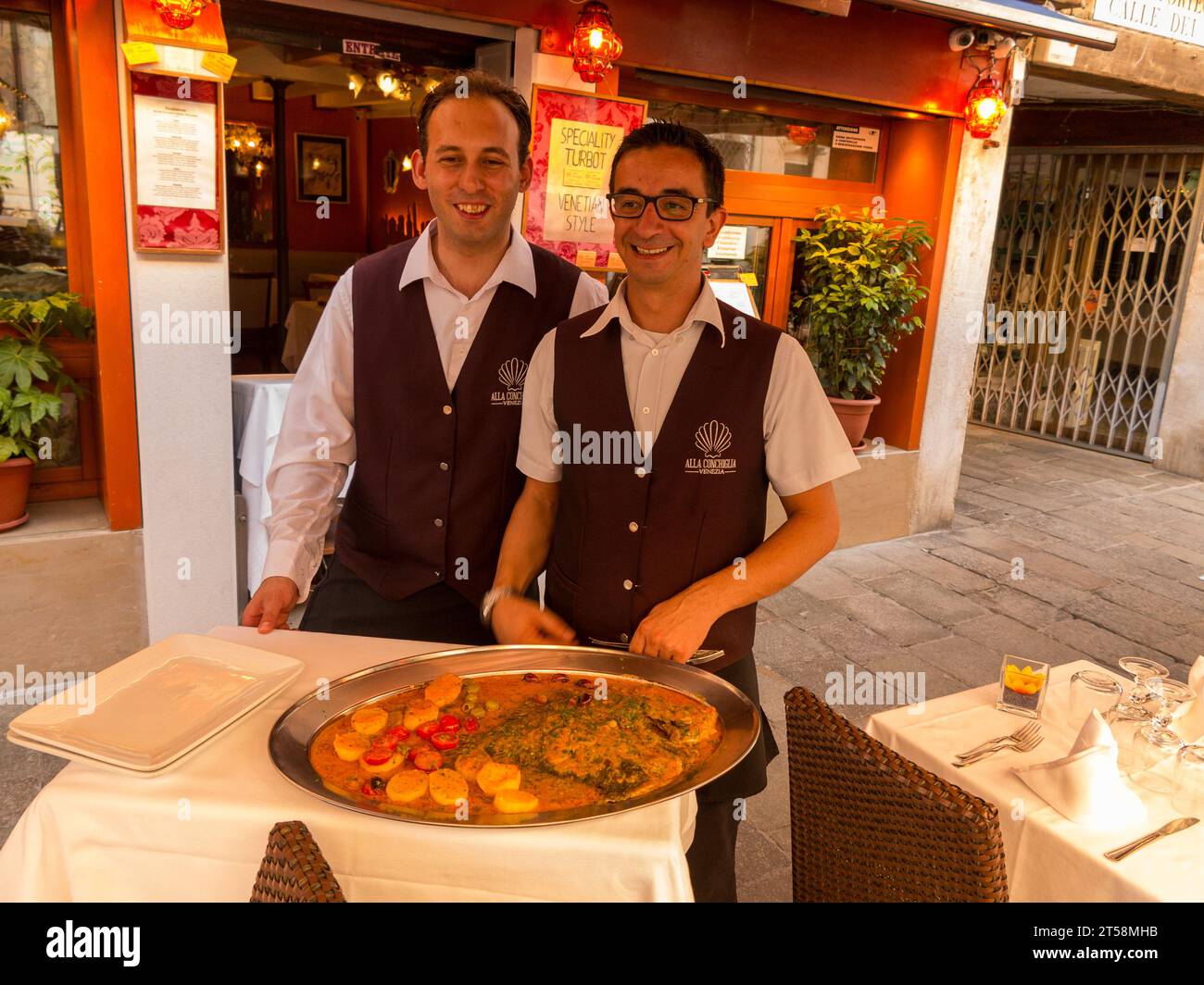 Serveurs au restaurant Alla Conchiglia à Venise, Italie. Ils sourient tout en présentant un plat de poisson. Banque D'Images