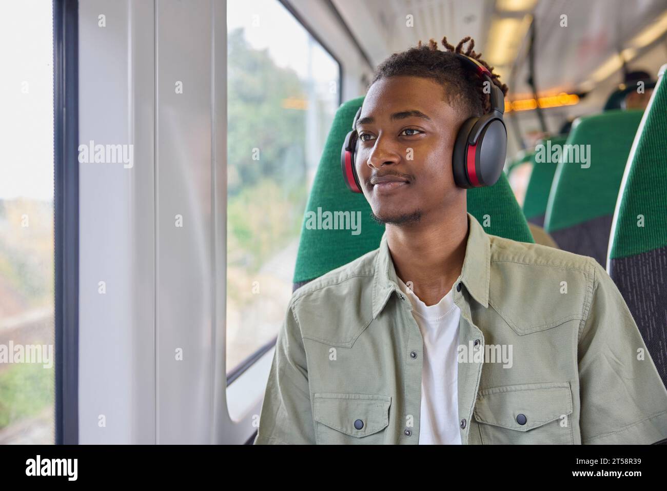 Jeune homme se rendant au travail assis dans un train portant un casque sans fil Banque D'Images