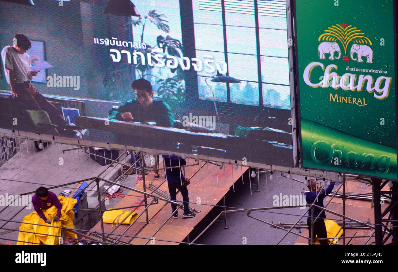 Vue de dessus. Des jeunes hommes assemblent les structures des stands du marché nocturne de Patpong, sur la route 1 de Patpong, dans le district de Silom. Bangkok, Thaïlande. Les stands sont assemblés à 3h et démontés vers 1h tous les jours. Un panneau lumineux au-dessus des travailleurs, panneau permanent pour annoncer des boissons de marque Chang à côté de cela. Banque D'Images