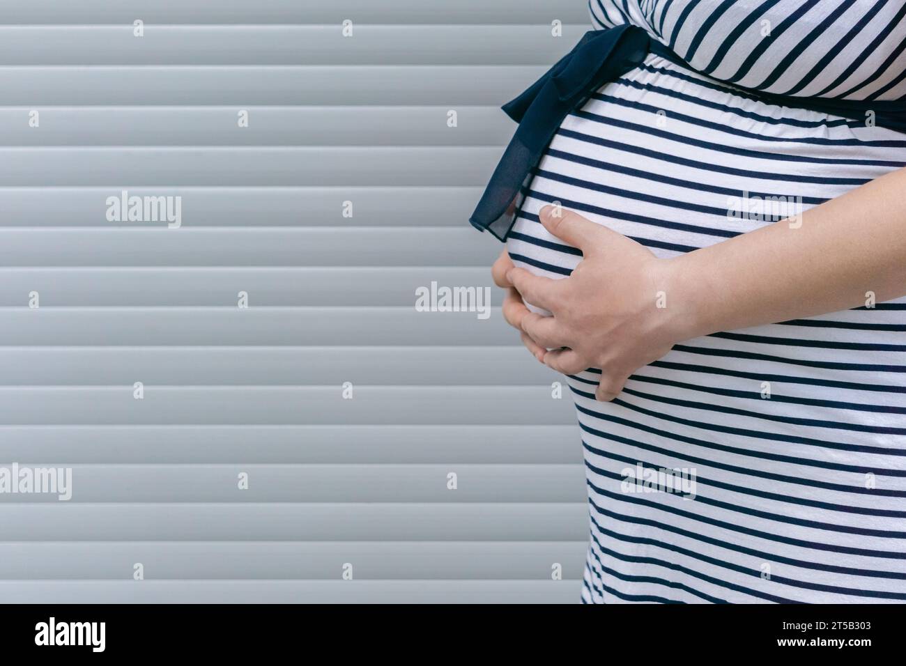 Ventre de femme enceinte en fond rayé. Femme enceinte touchant doucement son ventre et se souciant de sa santé. Banque D'Images