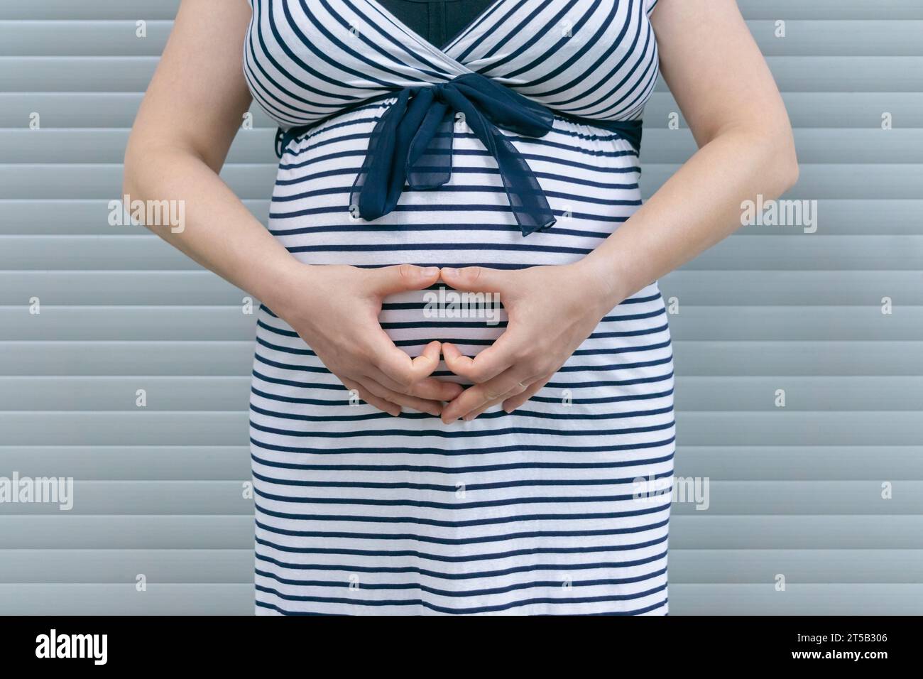 Femme enceinte montrant un signe de cœur sur son ventre. Femme enceinte debout sur fond rayé Banque D'Images