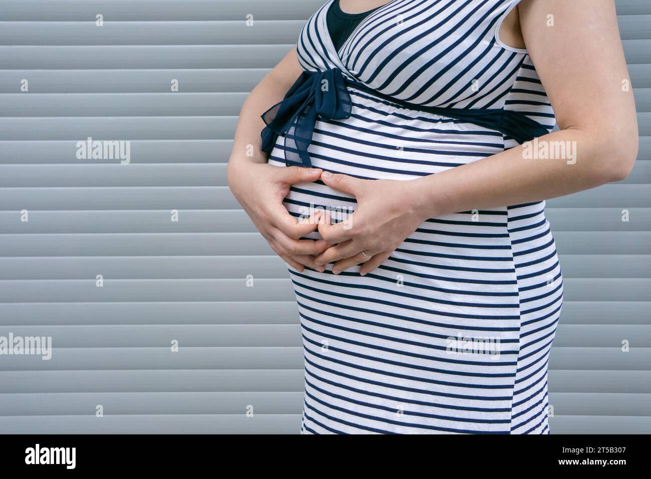 Femme enceinte debout sur fond rayé. Ventre de femme enceinte avec signe de coeur. Banque D'Images