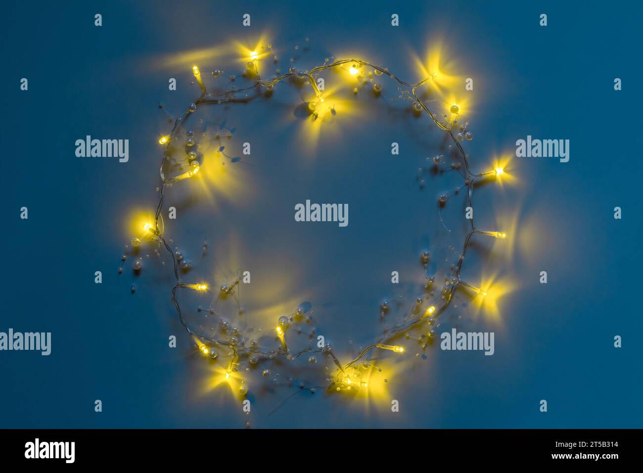 Petite guirlande lumineuse de forme ronde sur fond bleu. Cadre pour texte avec décoration de Noël. Guirlande de Noël éclatante. Lumières festives comme symbole Banque D'Images
