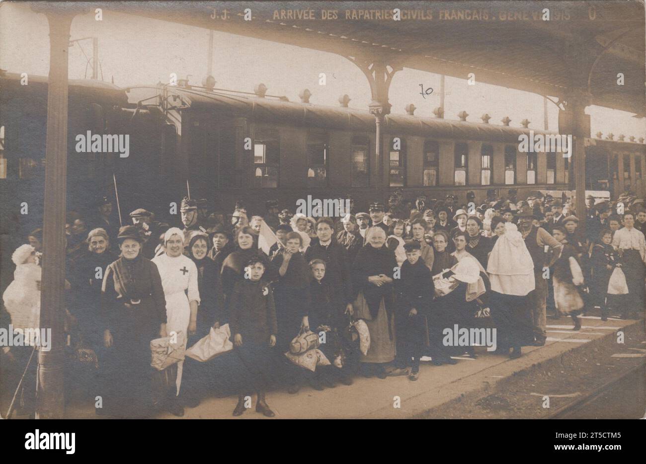 'Arrivée des réfugiés civils français, Genève 1915' / 'arrivée des rapatriés civils Français, Genève 1915' : grand groupe de personnes sur un quai de gare, à côté d'un train. La plupart des passagers sont des femmes et des enfants. Une infirmière, vêtue de blanc avec une croix rouge sur son uniforme, se tient debout vers l'avant. Certaines personnes transportent des paquets de biens. Une personne tient un drapeau tricolore français. Banque D'Images