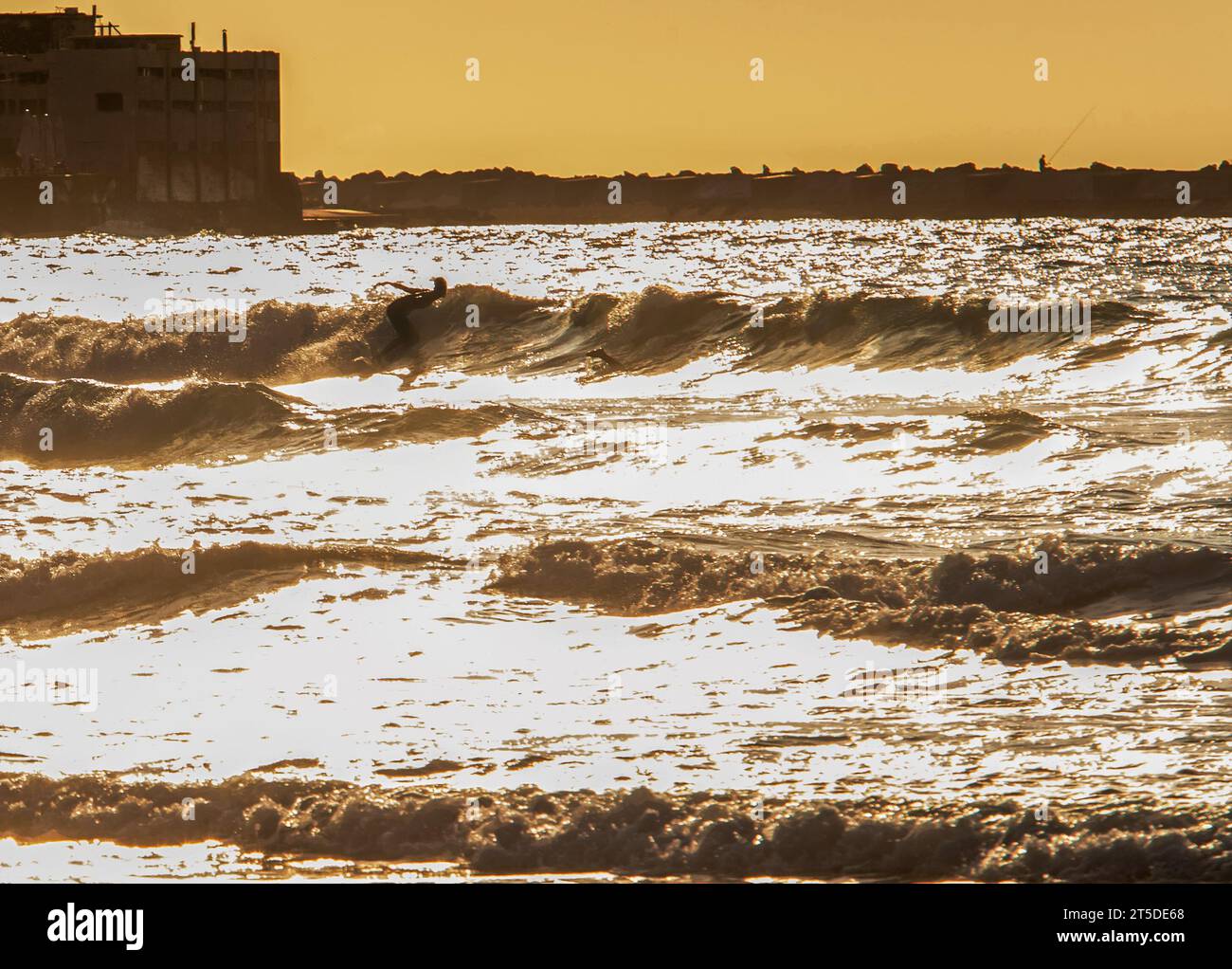 Silhouette de surfeur allant à cheval dans l'eau du golfe de Gascogne dans le sable mouillé brillant. Une personne marche avec une planche (surf) sur du sable mouillé dans l'eau Banque D'Images