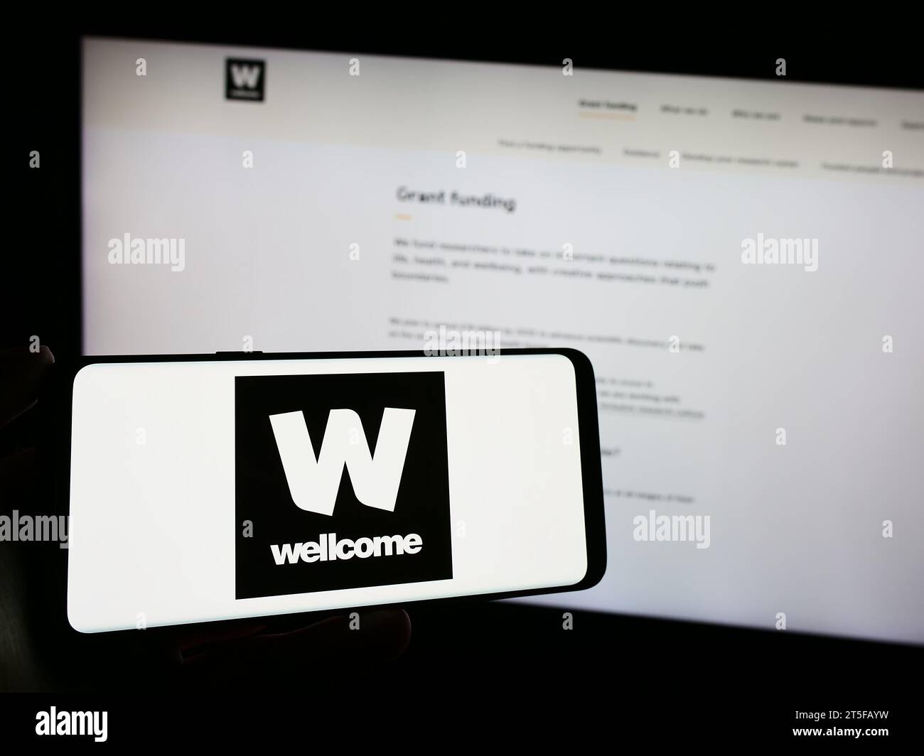 Personne tenant un téléphone portable avec le logo de la fondation caritative britannique Wellcome Trust devant la page Web. Concentrez-vous sur l'affichage du téléphone. Banque D'Images