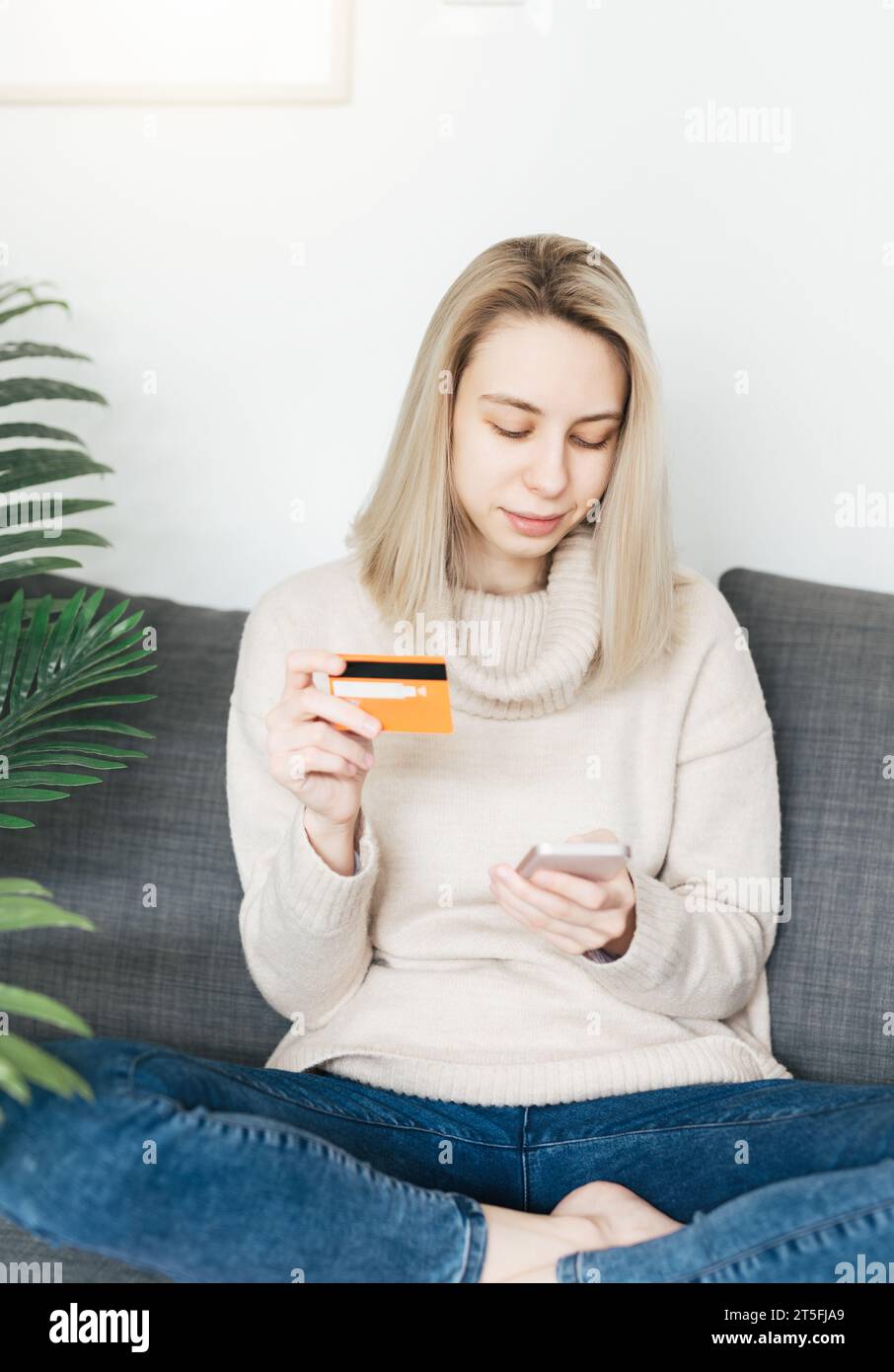 Jeune femme tenant un smartphone et une carte bancaire de crédit, impliquée dans le shopping mobile en ligne à la maison, heureuse femme achetant des biens ou des services Banque D'Images