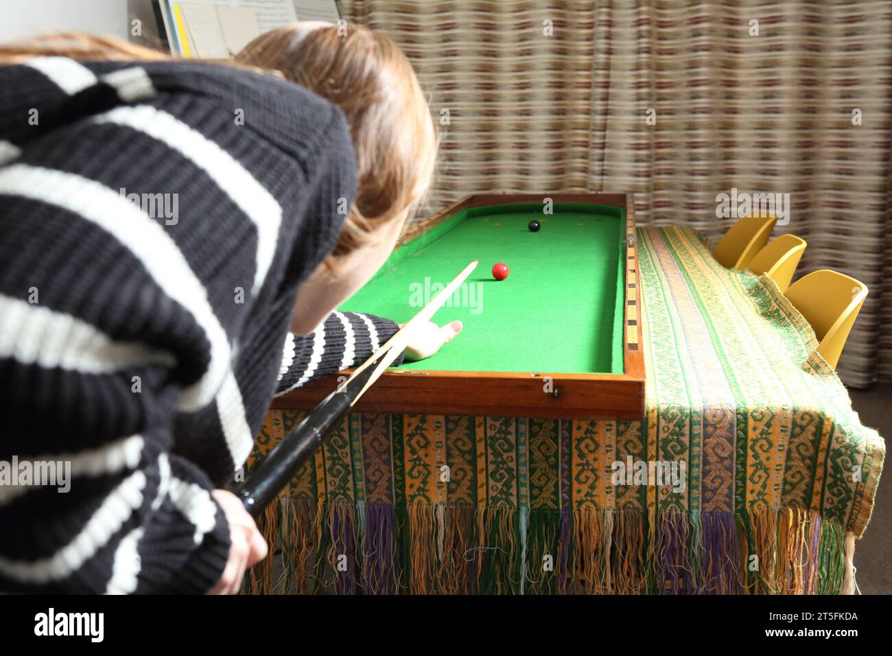 Adolescente jouant au jeu traditionnel de pub de bagatelle dans le salon à la maison - vue de son point de vue sur l'épaule. Banque D'Images