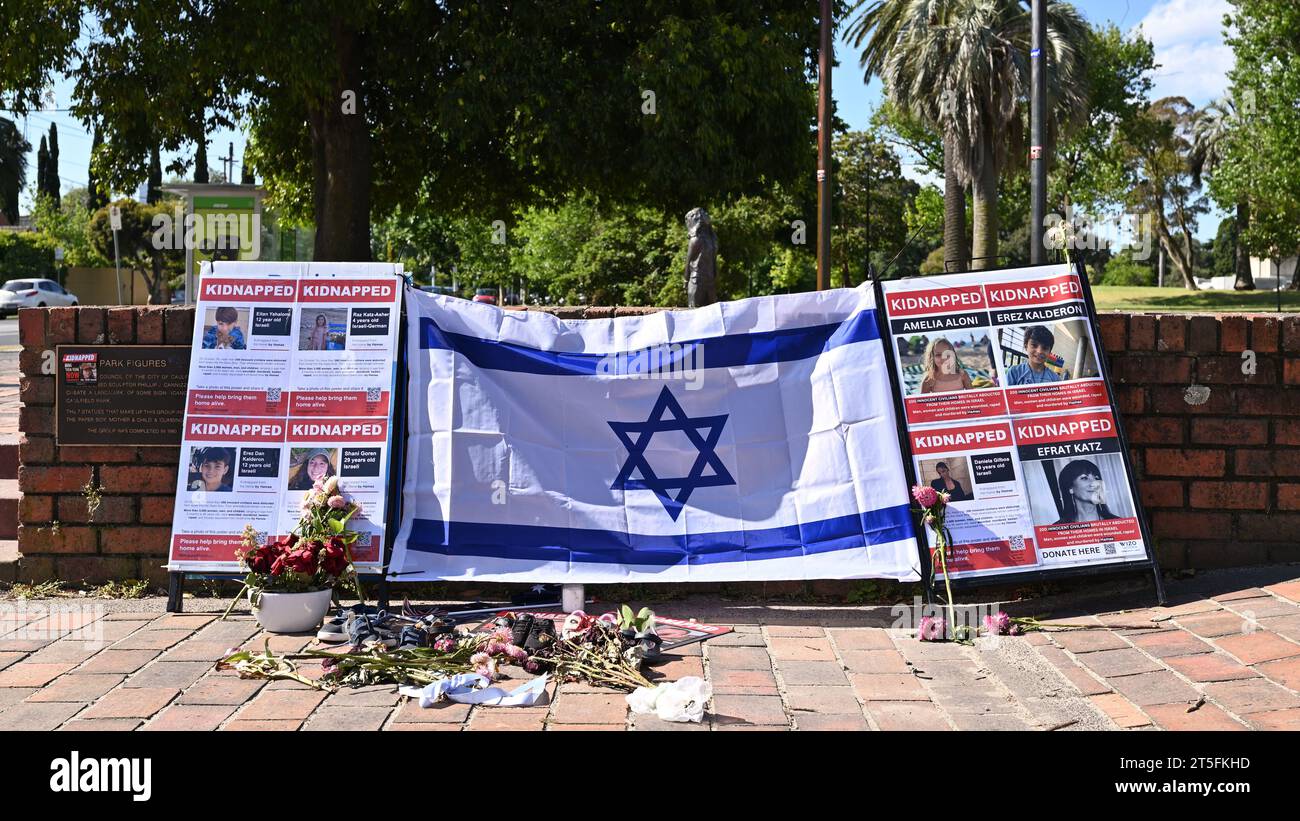 Des affiches représentant des personnes enlevées par le Hamas et un drapeau israélien à l'entrée du parc Caulfield de Melbourne, avec des fleurs disposées devant l'exposition Banque D'Images