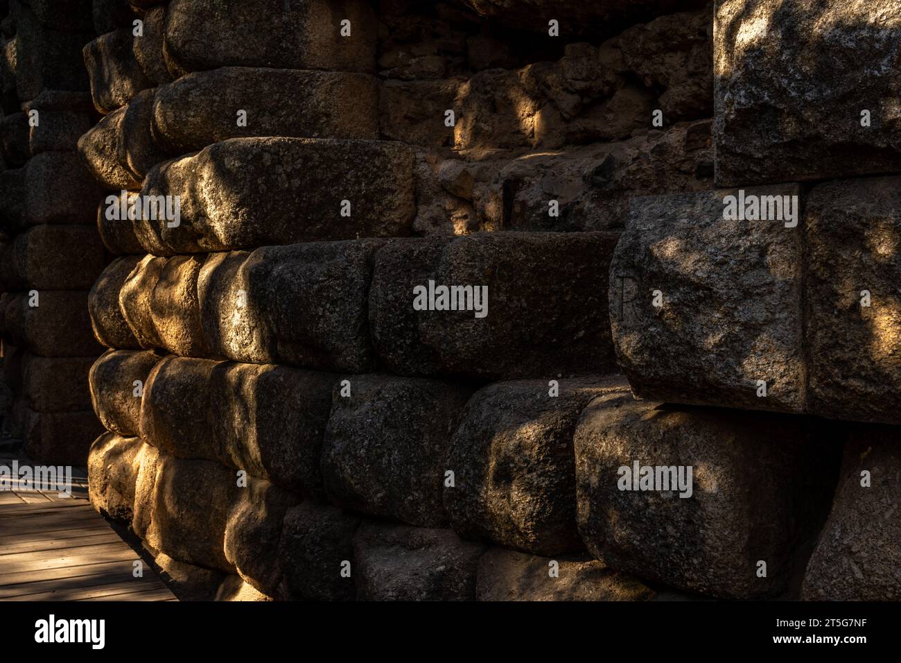 Blocs de pierre et de roche du mur entourant les escaliers de l'ancien théâtre romain de Mérida, avec la porte voûtée en arrière-plan illuminée Banque D'Images