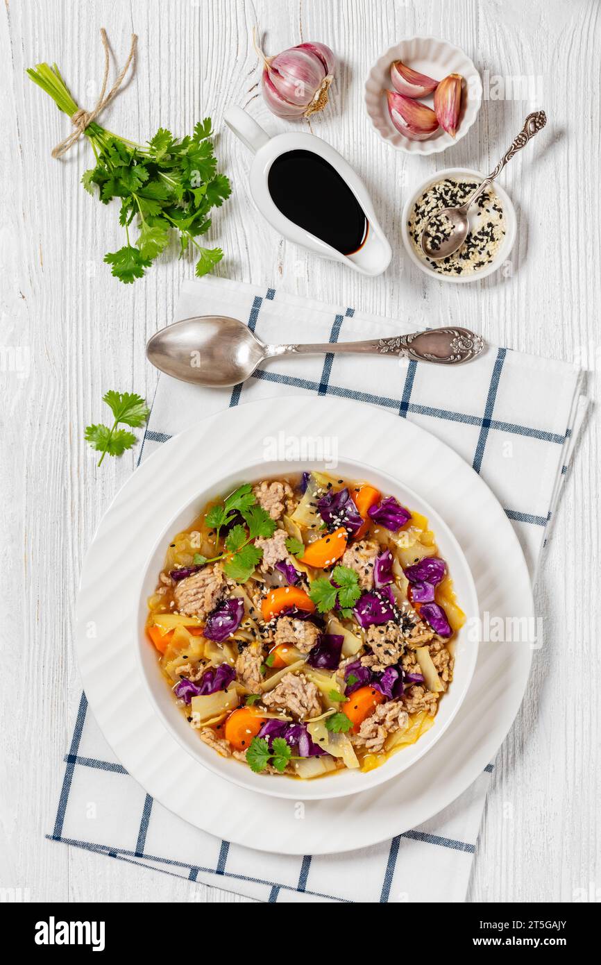 soupe au chou roulé aux œufs avec du porc haché et des légumes dans un bol blanc sur une table en bois blanc avec des ingrédients, cuisine asiatique, vue verticale d'en haut Banque D'Images