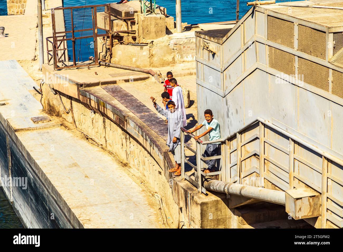 Les enfants égyptiens saluent joyeusement les navires de croisière qui traversent l'écluse d'Esna. Esna, Égypte - 20 octobre 2023. Banque D'Images