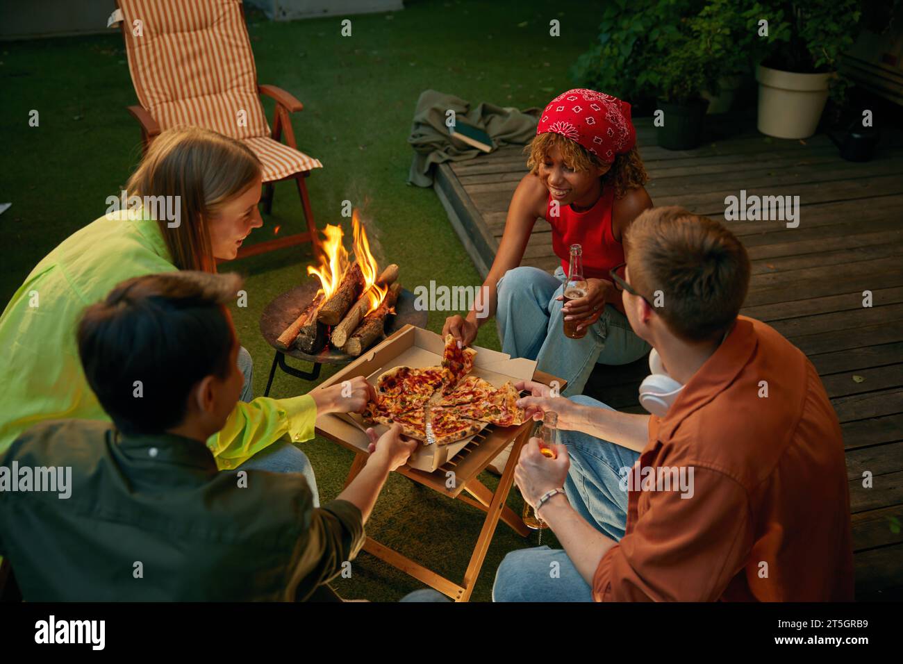 Amis heureux appréciant pizza et bière boire à proximité feu de camp Banque D'Images