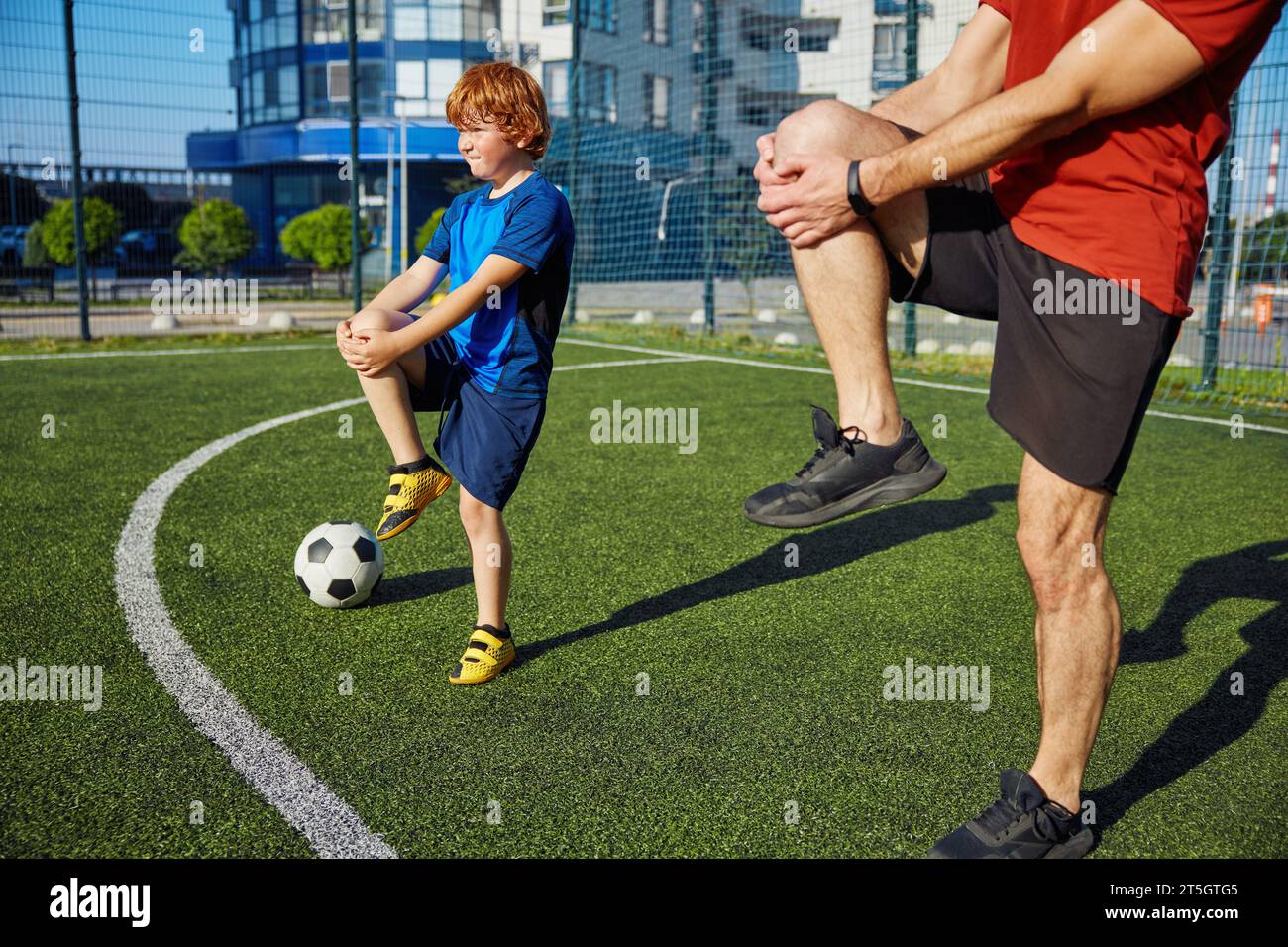 Papa et son fils font de l'entraînement physique et réchauffent les jambes avant l'entraînement de football Banque D'Images