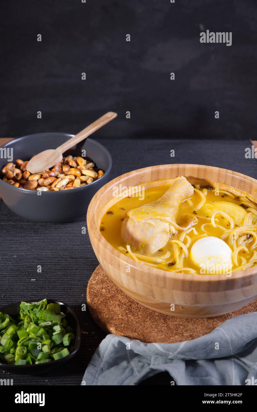 Plat typiquement péruvien connu sous le nom de soupe au poulet, dans un bol en bois avec citron et ciboulette. Banque D'Images