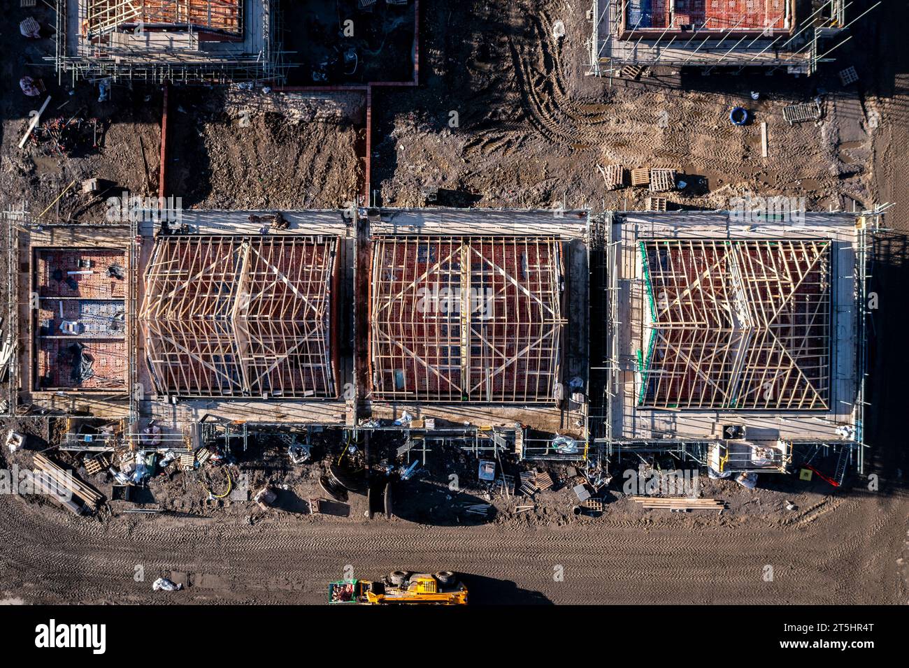 Vue aérienne directement au-dessus d'un chantier de construction avec de nouvelles maisons écoénergétiques construites avec les chevrons de toit exposés et entourés de scaf Banque D'Images
