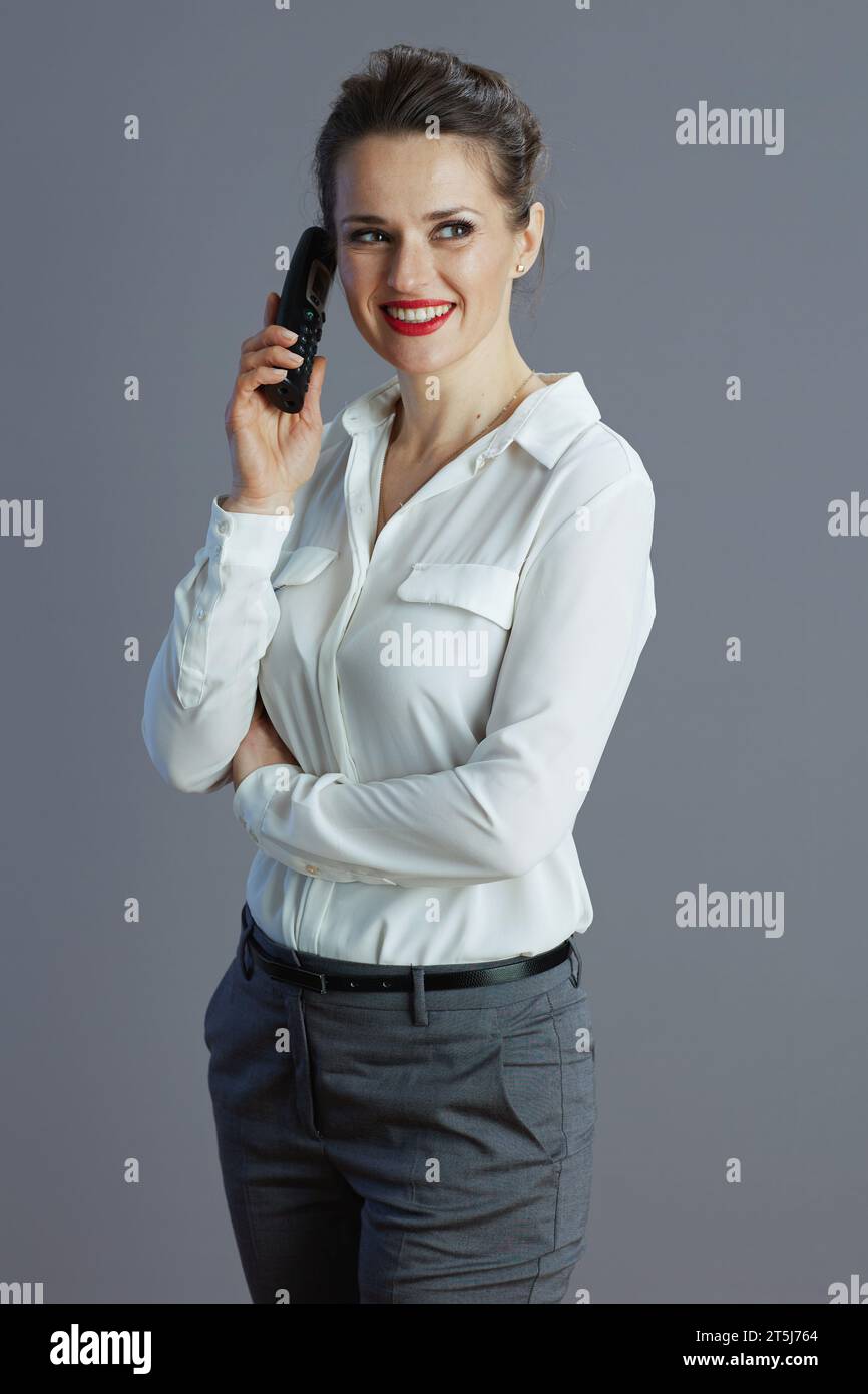 souriant femme élégante travailleur en chemisier blanc parlant sur le vieux téléphone radio sur fond gris. Banque D'Images