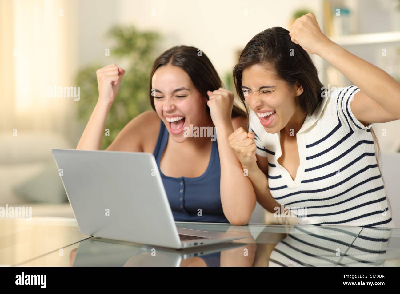 Deux amis enthousiastes célébrant les nouvelles sur ordinateur portable ensemble à la maison Banque D'Images