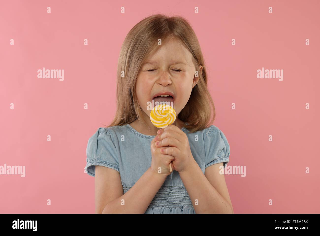 Jolie fille léchant sucette sur fond rose Banque D'Images