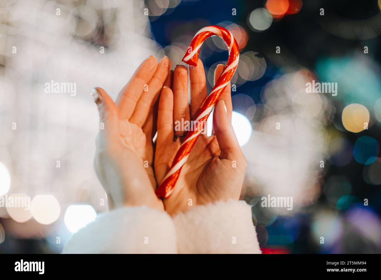 Détails de fée de vacances de Noël. Mains féminines tenant rouge blanc canne sucrée sucrée sucrée sucrée sucrée sur le fond de l'éclairage magique bleu argent. Banque D'Images