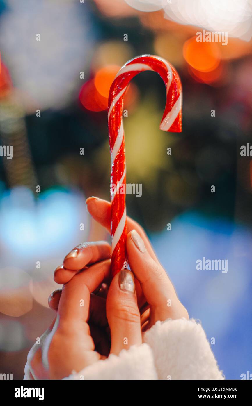 Détails de fée de vacances de Noël. Mains féminines tenant rouge blanc canne sucrée sucrée sucrée sucrée sucrée sur le fond de la lumière bleue de bokeh. Banque D'Images