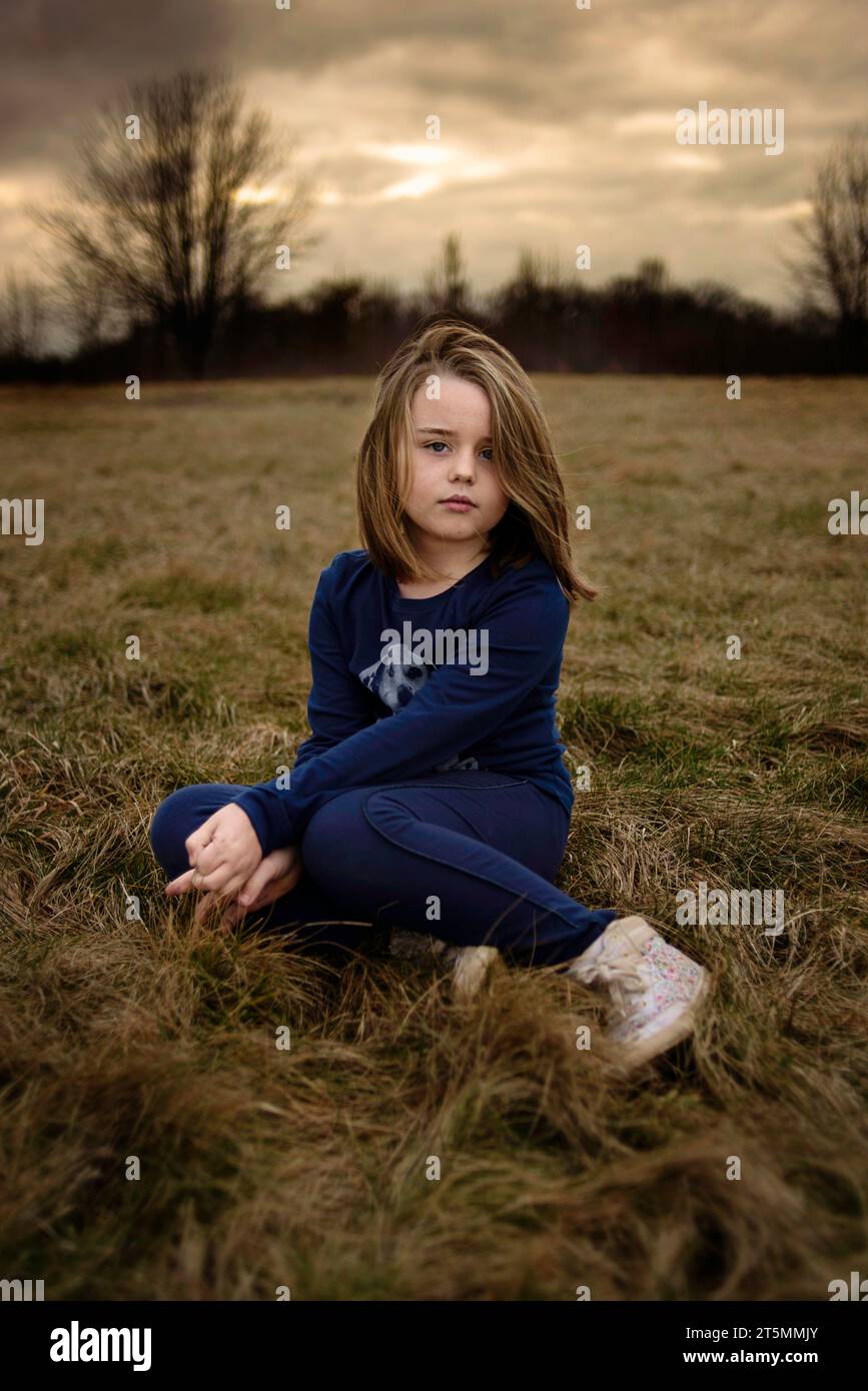 Belle jeune fille assise dans le champ au coucher du soleil Banque D'Images