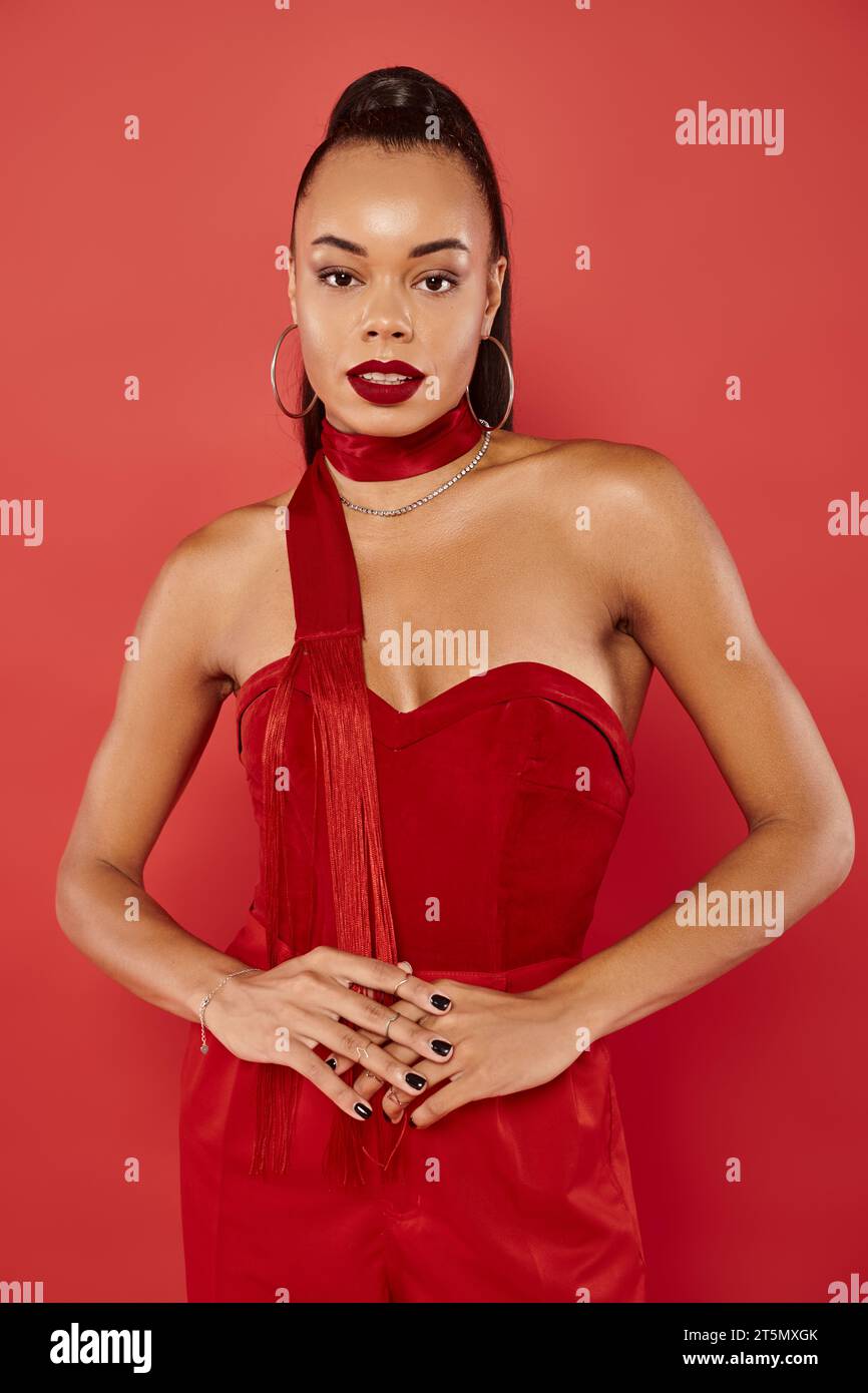 jolie femme afro-américaine dans haut vibrant sans bretelles et pantalon posant sur fond rouge Banque D'Images