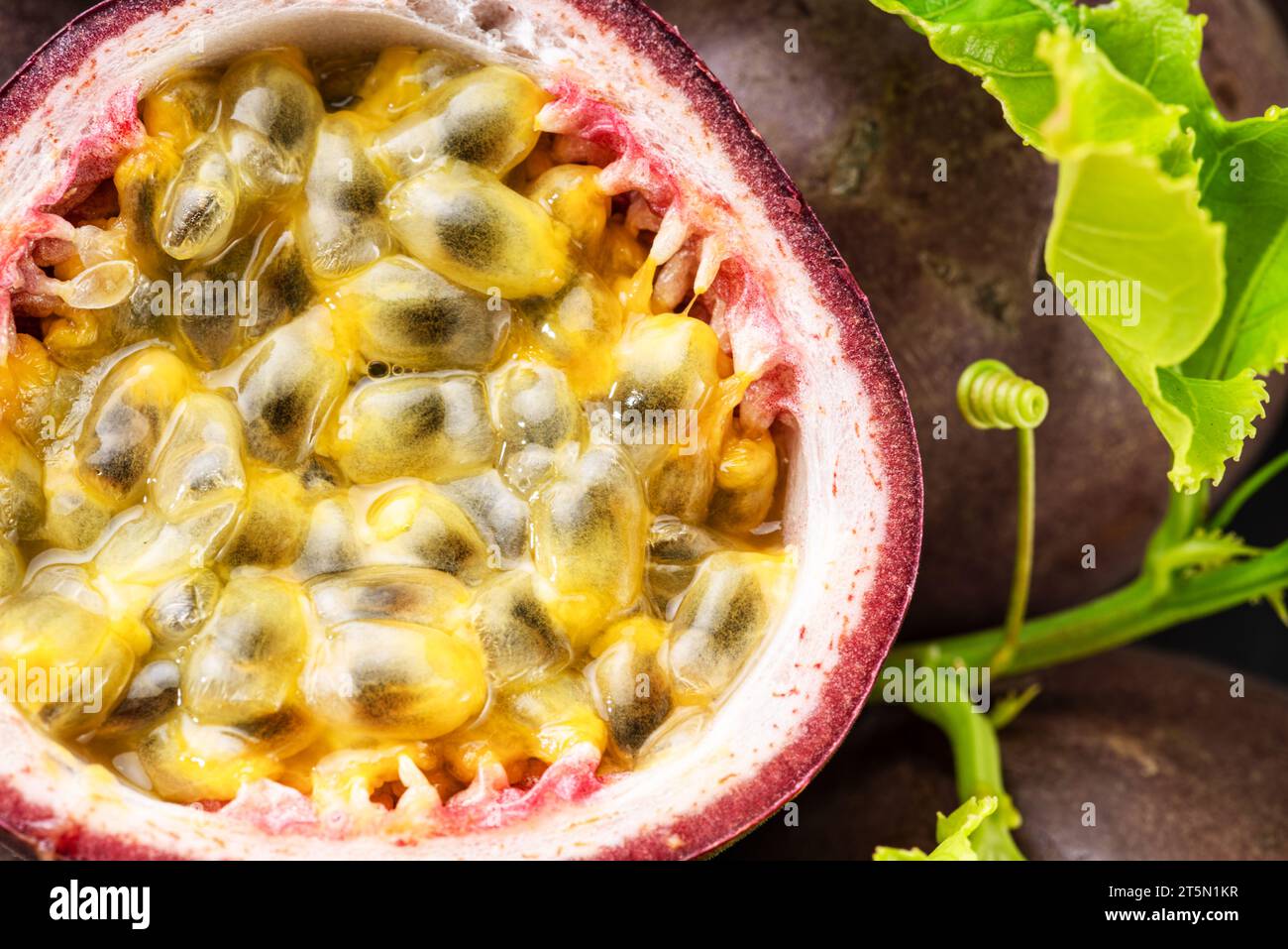 Fruits de la passion mûrs avec des graines de fruits de la passion et des feuilles de fruits de la passion sur une table en pierre grise. Joli fond de fruits exotiques pour vos projets. Banque D'Images