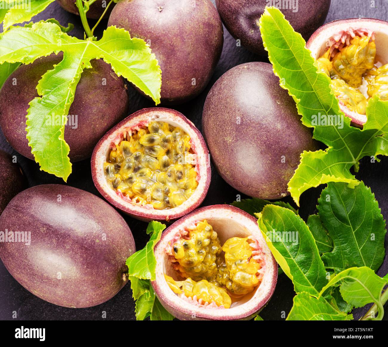 Fruits de la passion mûrs avec des graines de fruits de la passion et des feuilles de fruits de la passion sur une table en pierre grise. Joli fond de fruits exotiques pour vos projets. Banque D'Images