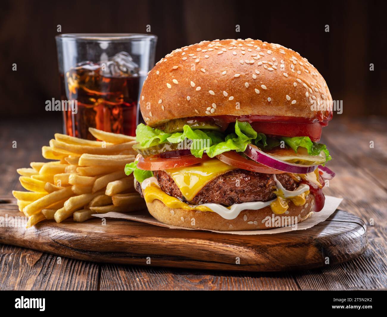 Cheeseburger ou hamburger savoureux, verre de cola et frites sur plateau en bois gros plan. Banque D'Images