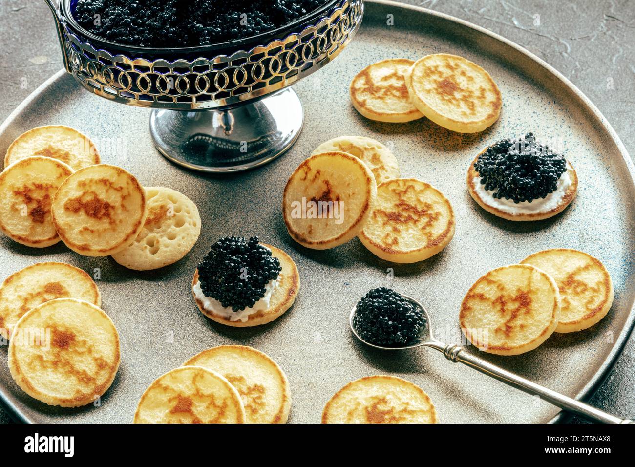 Blinis au caviar noir et fromage à la crème, sur un plat festif sur fond noir, mini crêpes, un élégant apéritif Banque D'Images