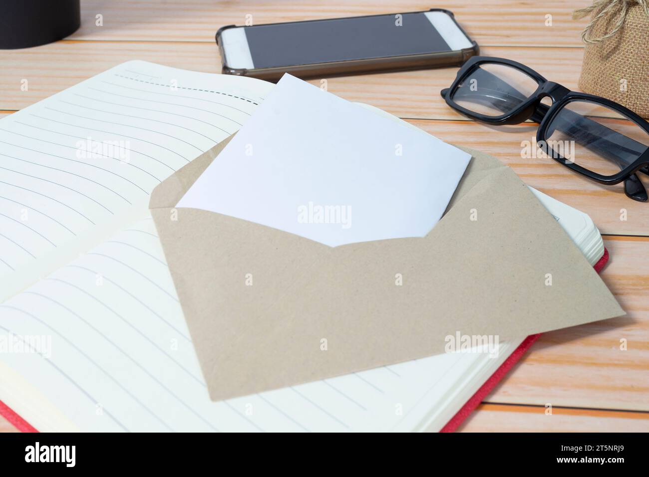 Carte dans enveloppe marron avec bloc-notes, smartphone, lunettes de lecture sur bureau en bois. Espace de copie. Banque D'Images