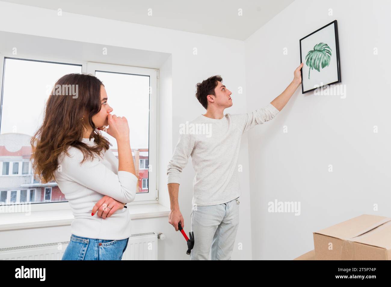 Femme regardant son petit ami accrochant le cadre photo mur blanc Banque D'Images